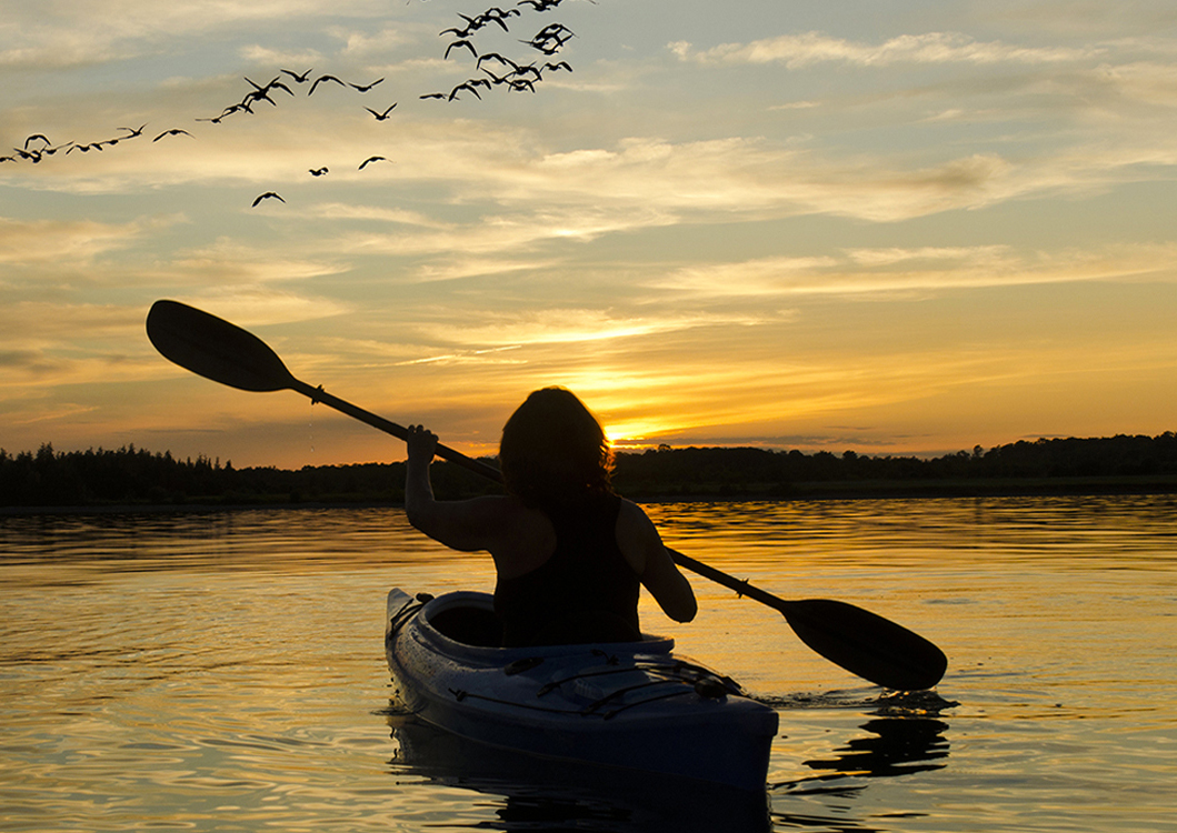 sillouette of woman kayaking into the sunset