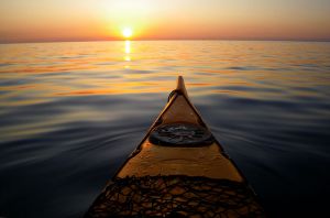 front of kayak in water facing sunset on horizon