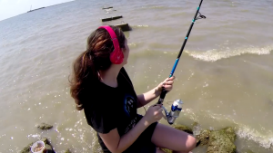 young girl with headphones sits on rock fishing